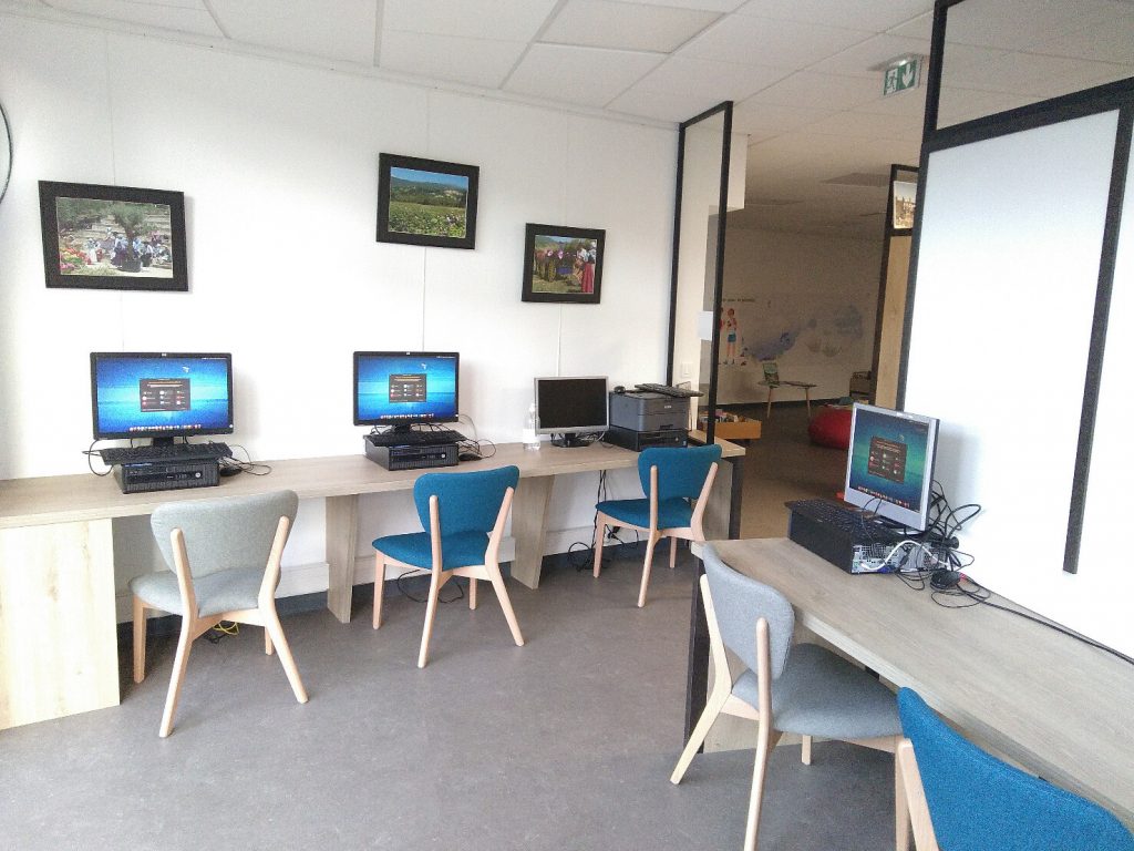 Vue d'une salle avec deux tables sur lesquelles sont installées des ordinateurs allumés avec la page d'accueil de EmmabuntüsDE4